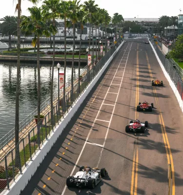 race cars zoom down a palm-tree lined street in St. Pete for the St. Pete Grand Prix