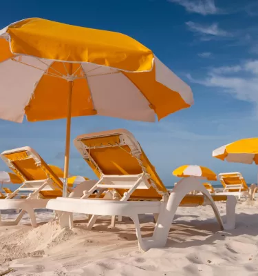 yellow and white beach umbrellas over yellow beach chairs on a white sand beach