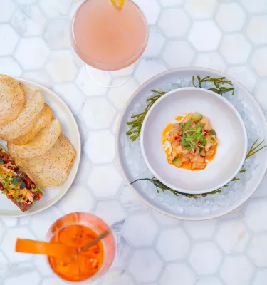 two cocktails and two appetizers set on a table with small white hexagonal tiles
