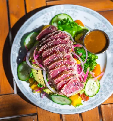 a fresh green salad with thin slices of raw ahi tuna decorated with sesame seeds on a blue and white china plate