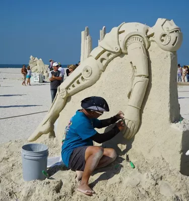Artist on the beach making a sand sculpture