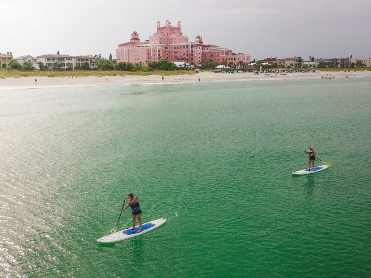 Two stand-up paddleboarders with the Don CeSar in the background