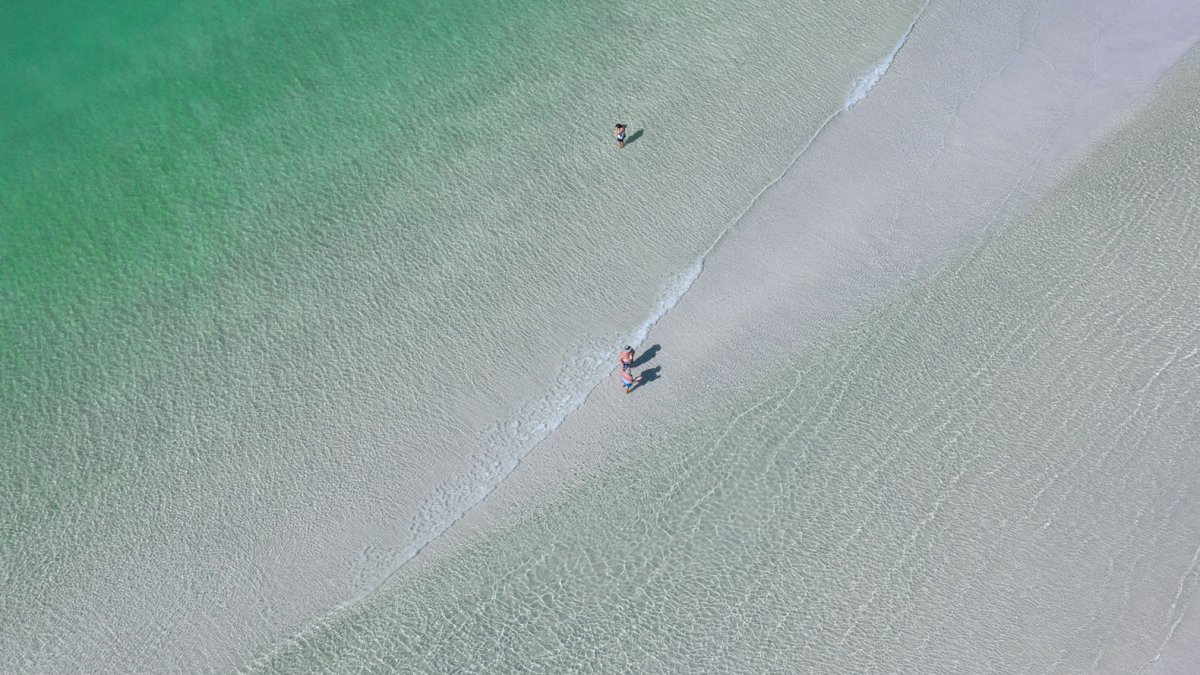 Aerial view of people walking in clear emerald-green water in Sunset Beach near St. Pete Beach, Florida
