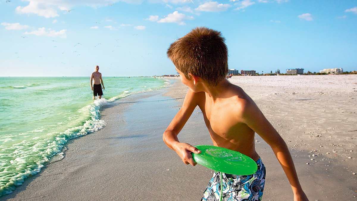 Um menino jogando frisbee com seu pai na praia em Treasure Island perto de St. Pete Beach