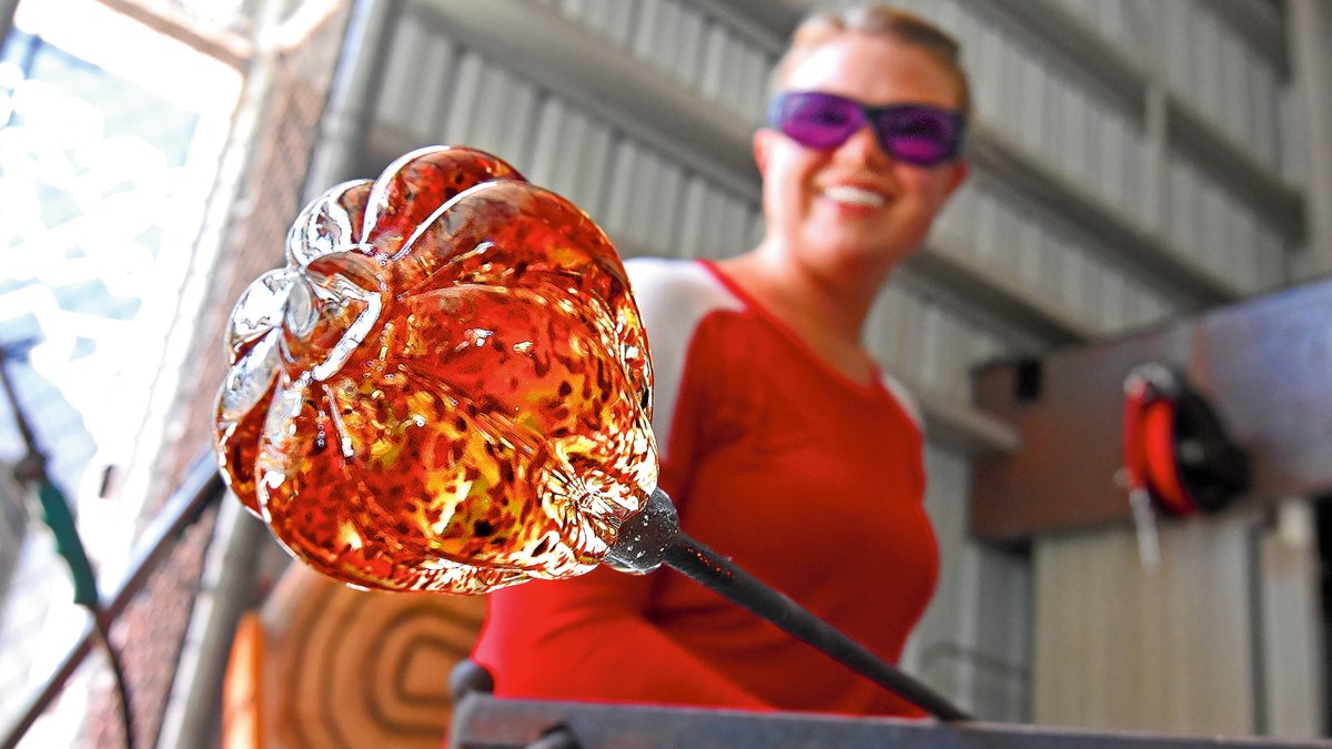 A glass artist holds a piece of glass over heat