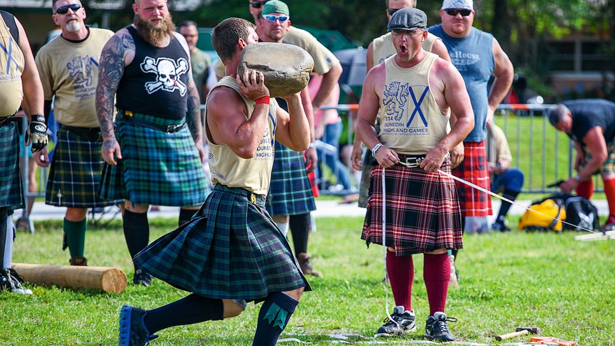 a young man in a kilt throws a rock while the crowd cheers at Dunedin's Highland Games