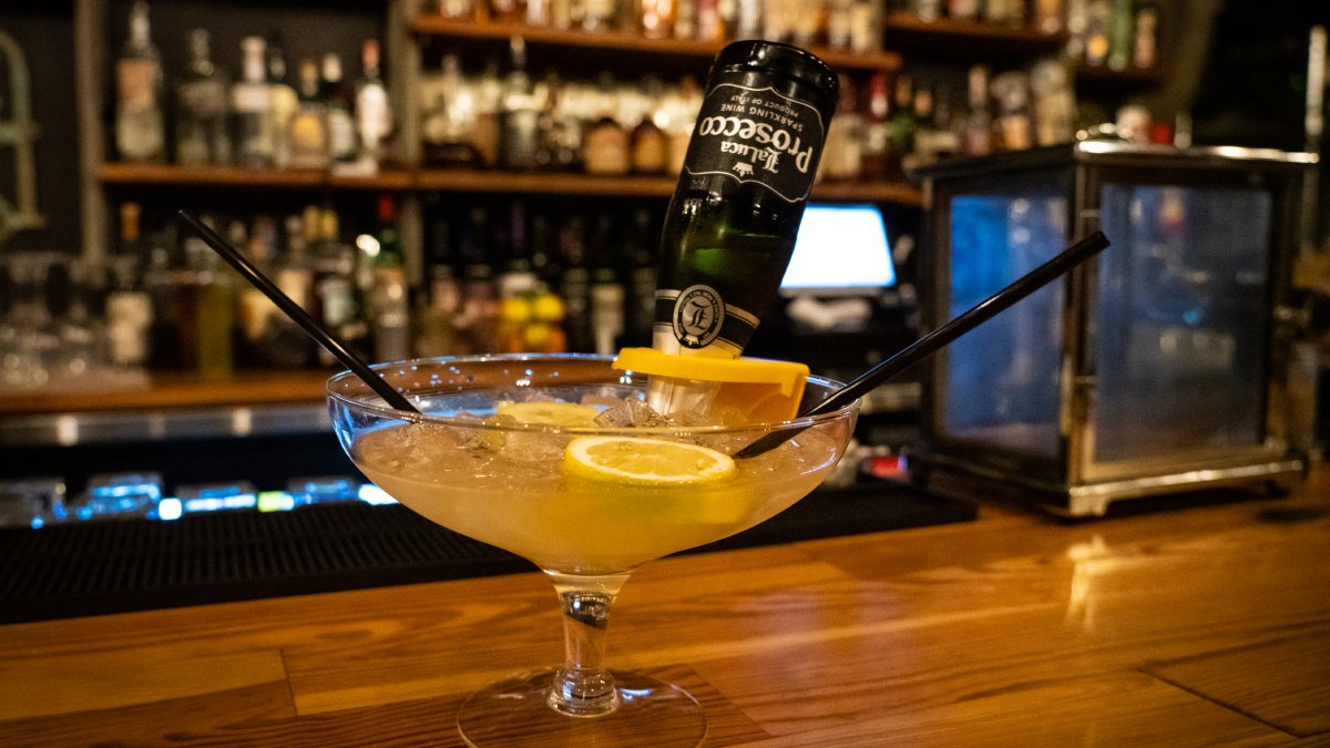 A yellow cocktail with lime and bottle of prosecco at the bar at Gigglewaters Bar