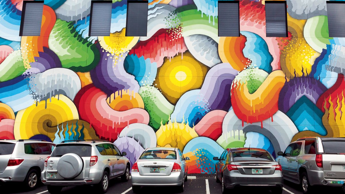 Several cars parked in front of a colorful mural