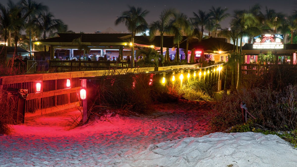 Una vista nocturna del bar de playa Jimmy B's, iluminado con luces rojas.