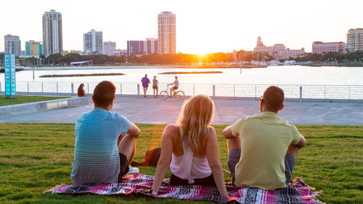 A group of friends seating in the grass field near the St. Pete Pier watching the sunset behind the buildings