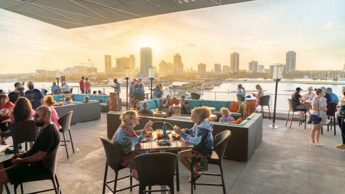 Several people enjoying drinks and meals while watching the sunset and St. Pete skyline from the rooftop of Pier Teaki.