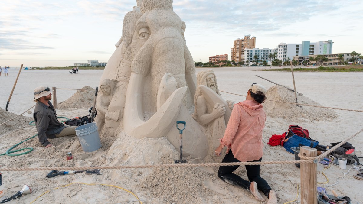 A woman sculpting a mammoth and a caveman out of sand at Sanding Ovations..