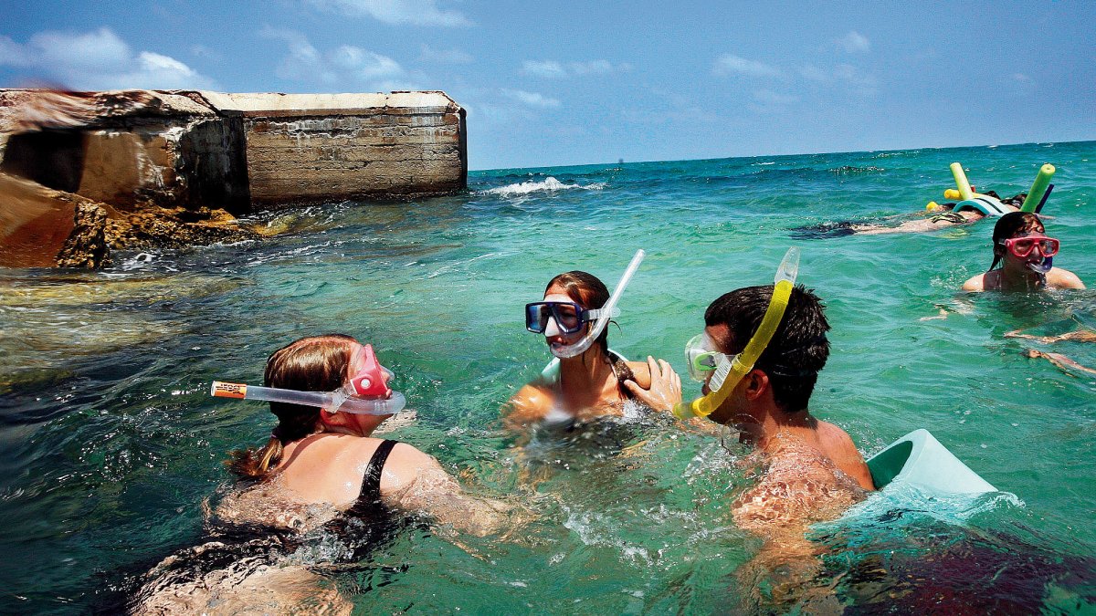 A group snorkeling in clear blue green water next to a fort.