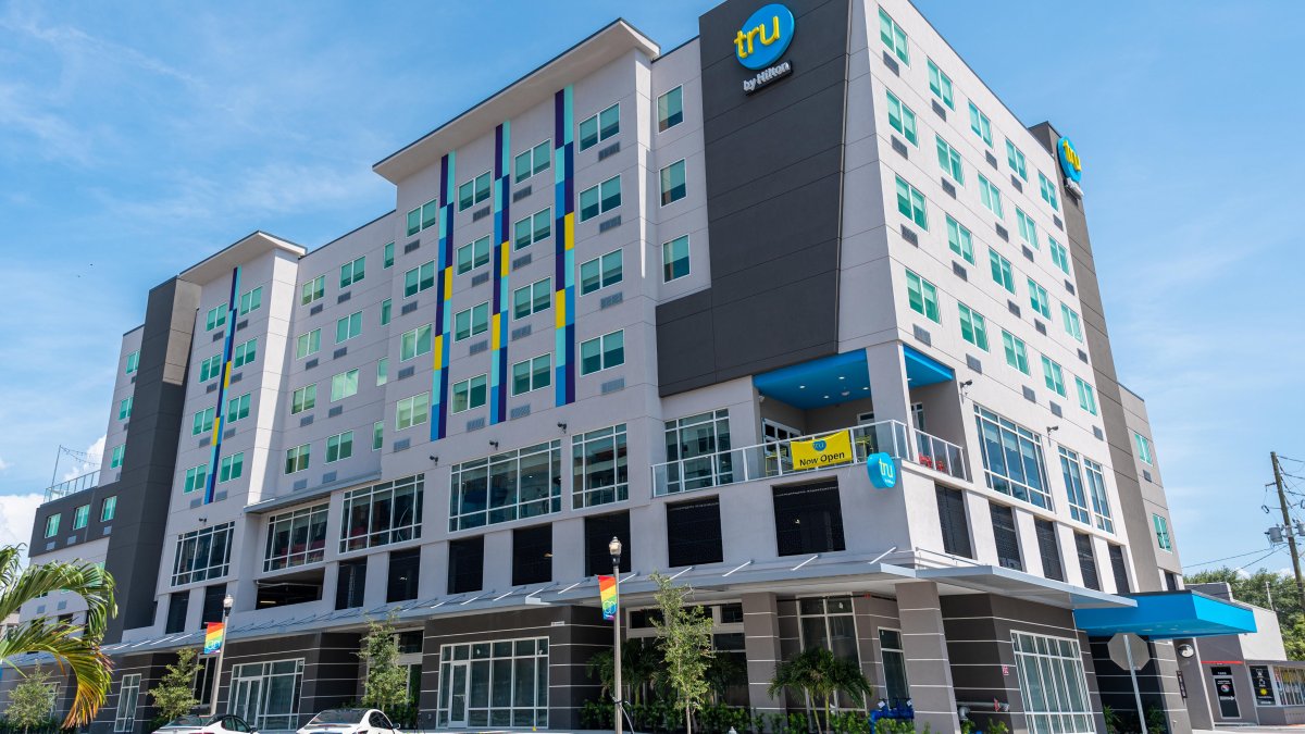 Exterior view of the hotel building. Accent colors yellow and blue on a white and gray building. There are rainbow banners at street level.