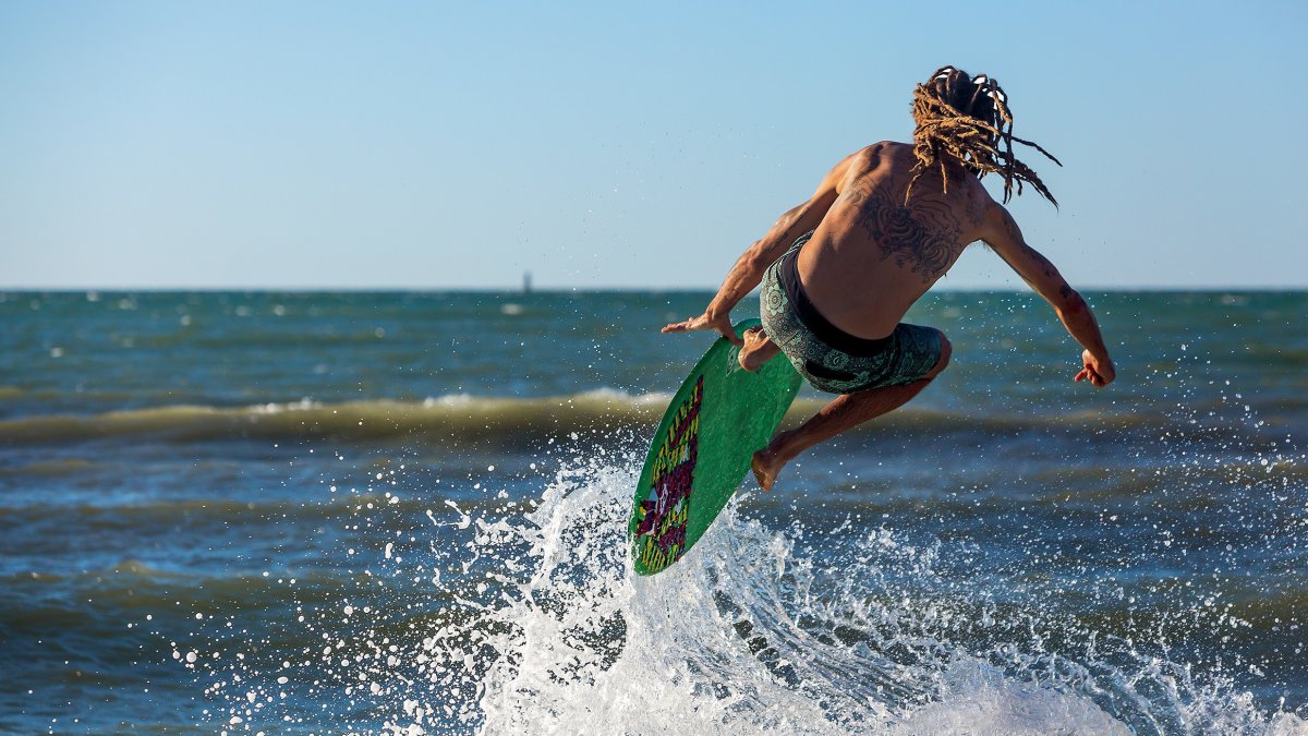 A man skimboards off the beach