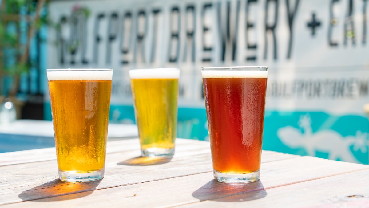 Three beer glasses with different color beers on top of an outside table of Gulfport Brewery.