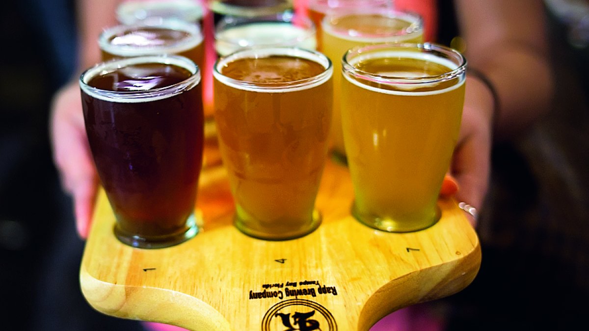 A lady wearing a pink shirt holding a beer sampler.