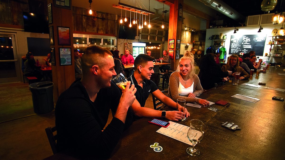 Three friends enjoying drinks at the bar at Crooked Thumb Brewery.