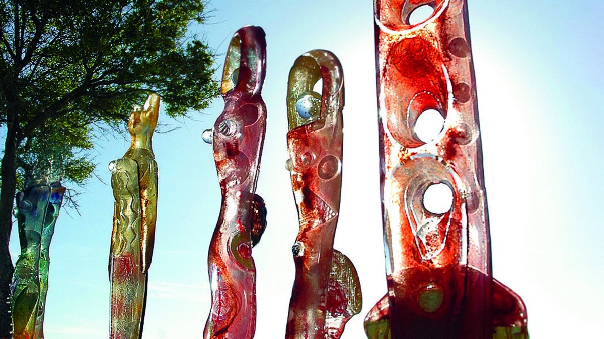 Five sculptures in a line next to a palm tree with the sunlight in the background.