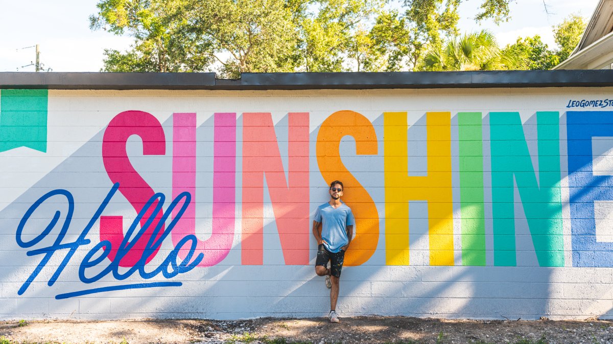 An artist stands in front of a mural that reads "Hello Sunshine"