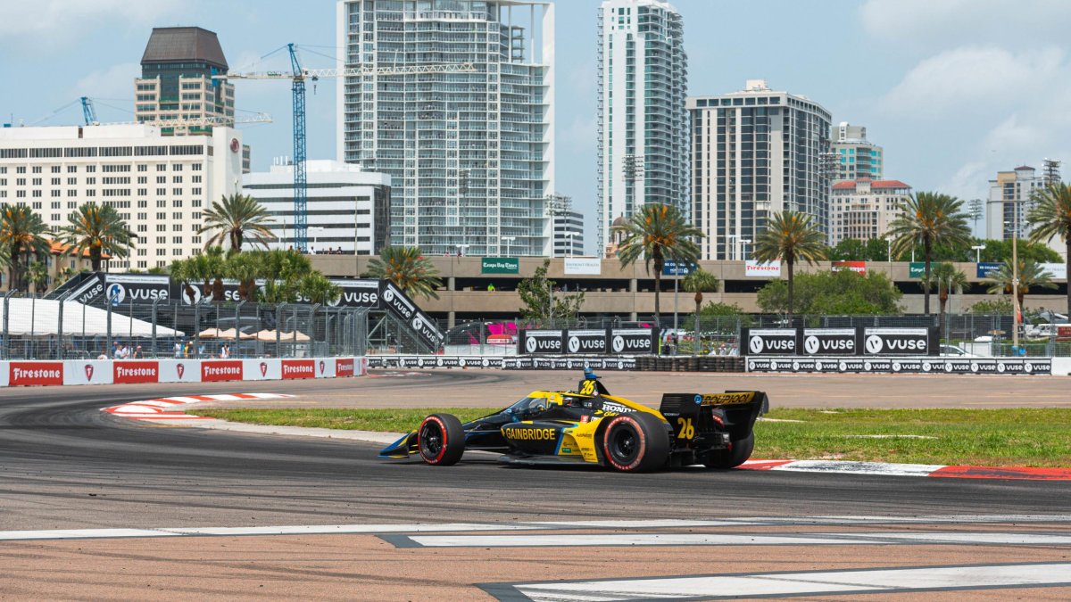 An Indy Car races along the track of the Firestone Grand Prix with the Saint Pete skyline in the background.