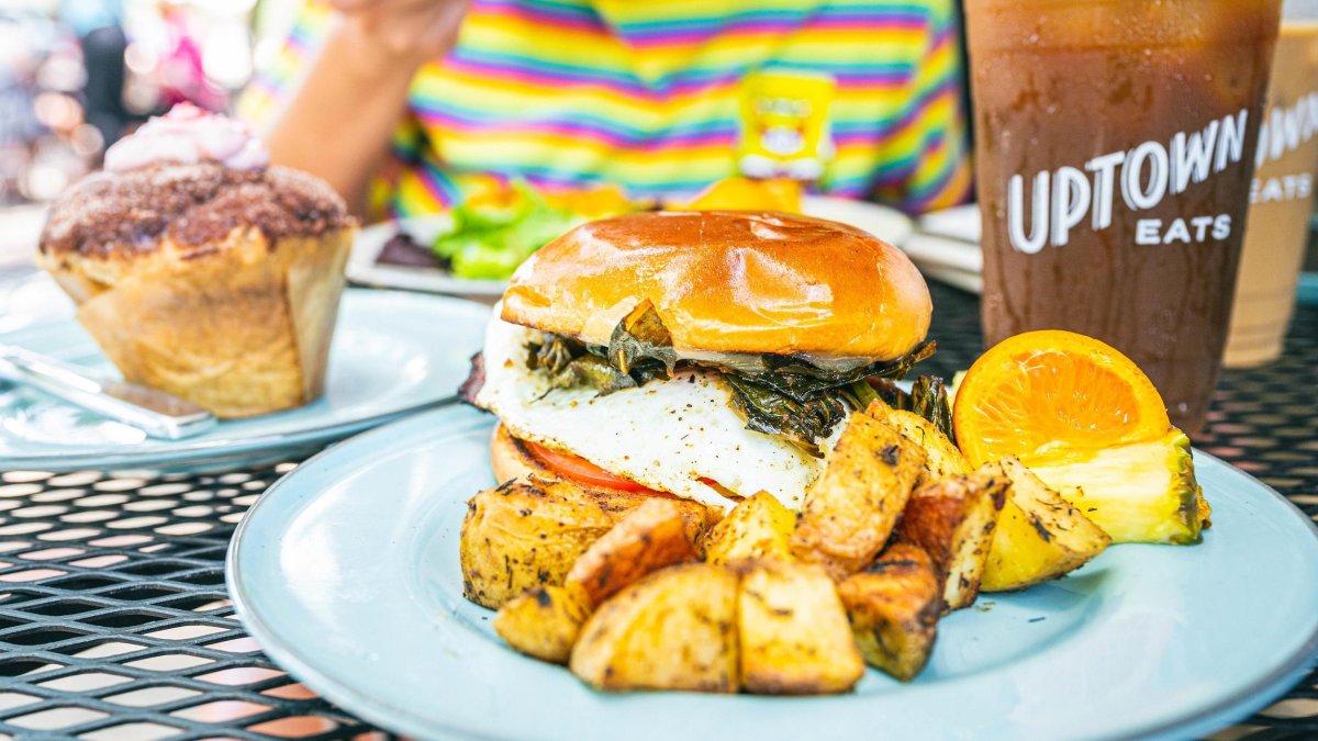 Food plates of an egg and spinach sandwich with roasted potatoes and a pastry.