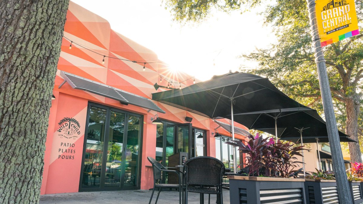 Exterior shot of Wild Child restaurant featuring decorated pink walls, black outside seating and trees.