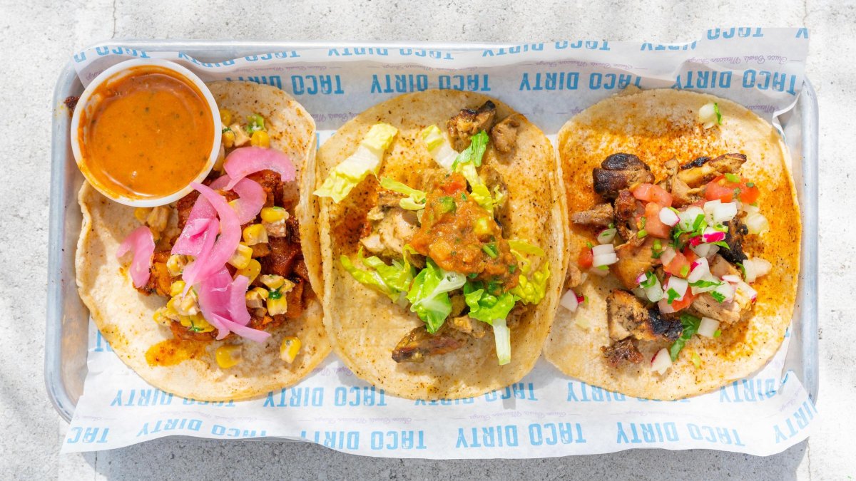 Three different tacos with topping on a horizontal tray with a side of salsa at Taco Dirty in St. Pete