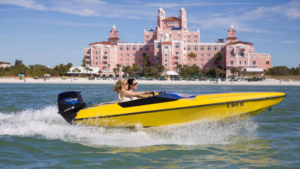 Two people in a yellow speedboat in front of the Don CeSar