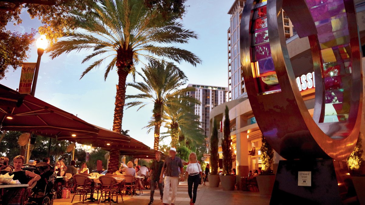 A family walks past diners at outdoor tables at Cassis in downtown St. Pete at dusk,