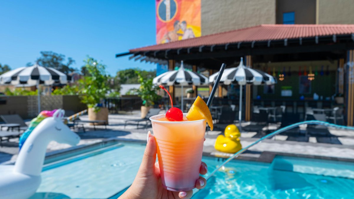 a woman's hand holding a fruity cocktail near the pool bar with umbrellas and a unicorn float at The Wet Spot in St. Pete