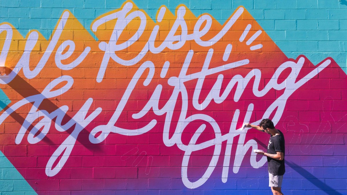 artist leo gomez paints a mural entitles we rise by lifting others