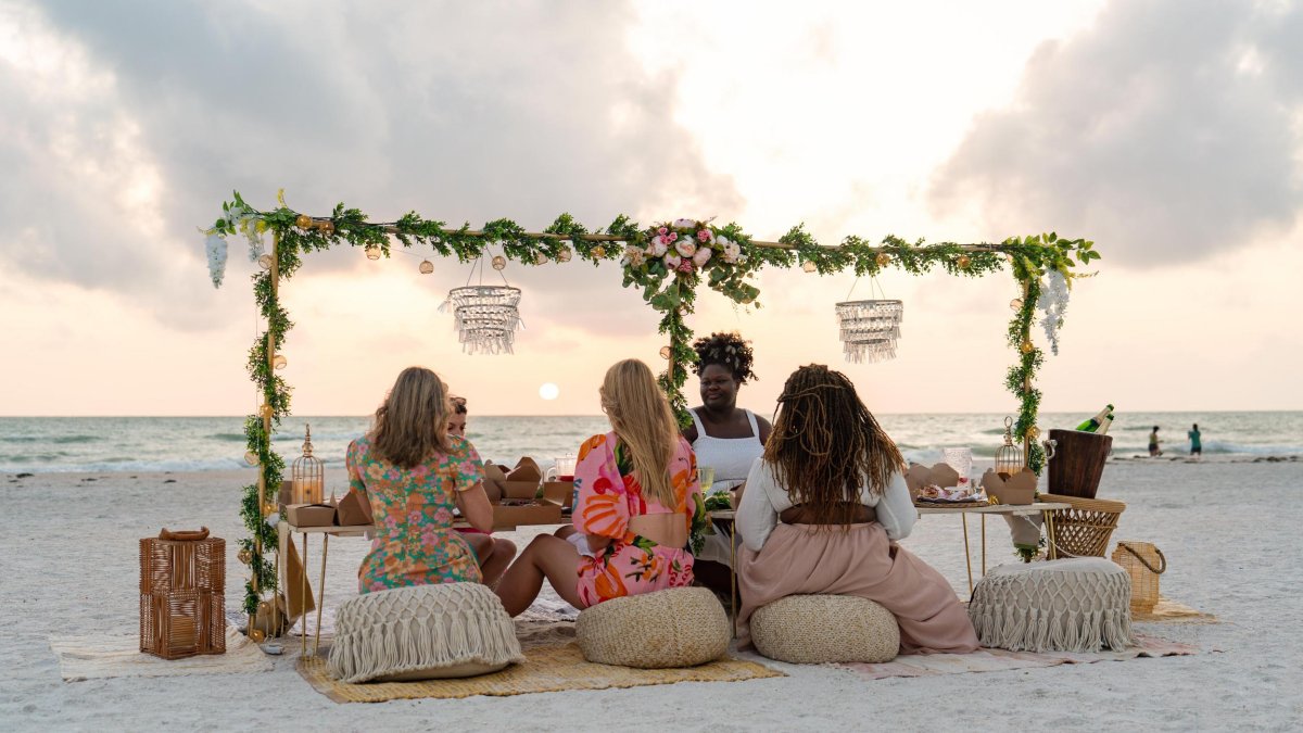 women enjoying a luxury beach picnic at sunset with flower garlands