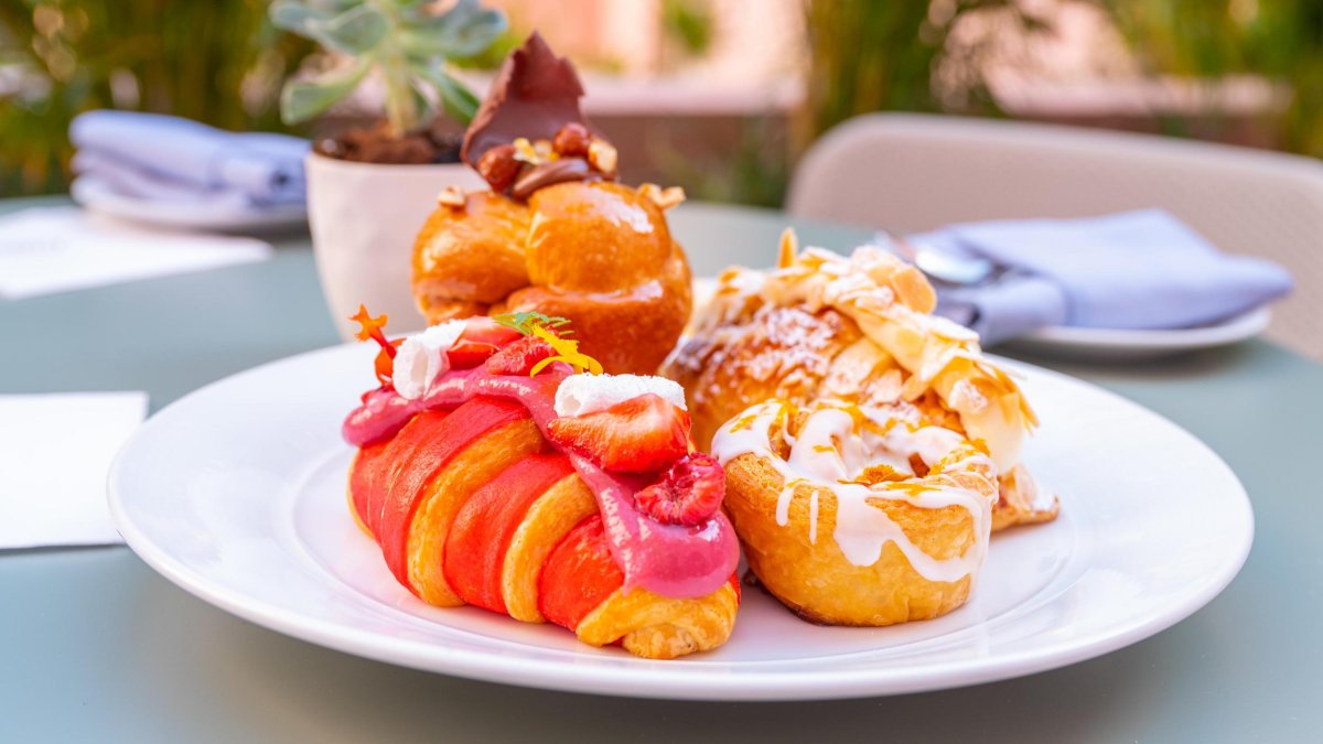 a pink croissant and other elaborate pastries with icing on a white ceramic plate