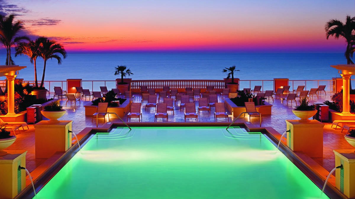 a bright pink orange sunset over a lighted pool and palm trees at the Hyatt Regency Clearwater Beach