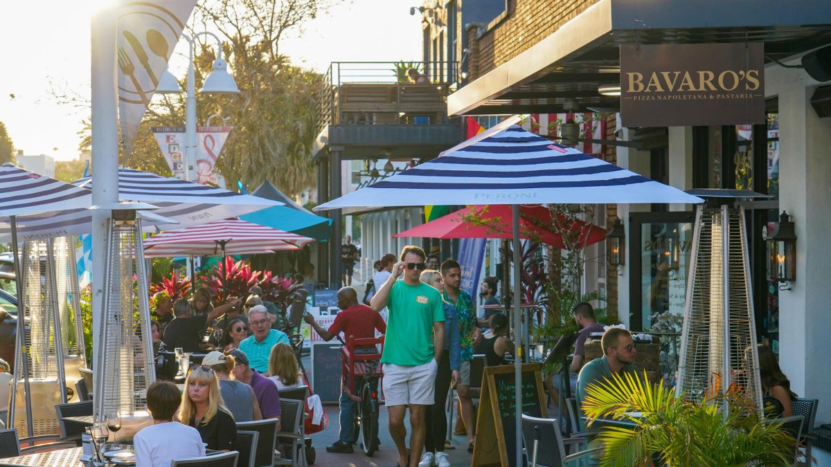 Pedestrians walk through sidewalk restaurant tables and umbrellas