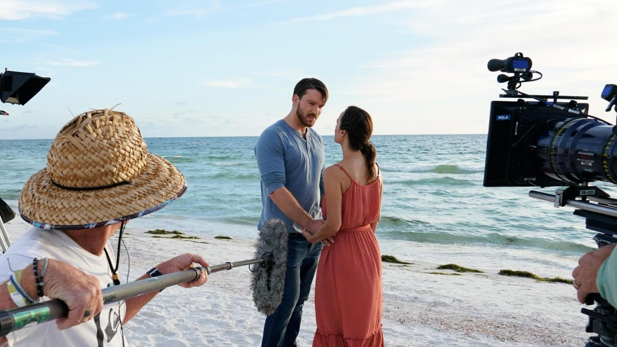 two actors hold hands on the beach while a crew films them for A Taste of Love, a Hallmark movie