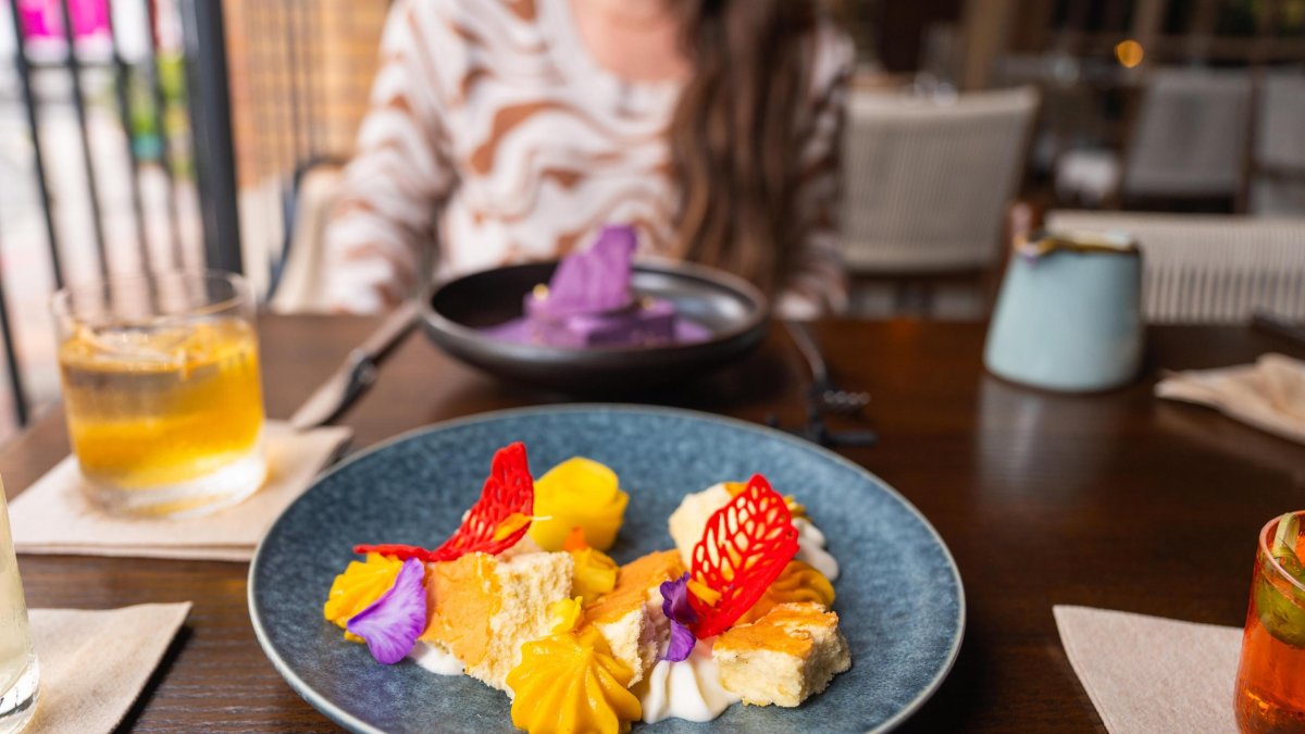 a colorful plate of food with cocktail surrounding it and a young woman in the background at Fortu restaurant