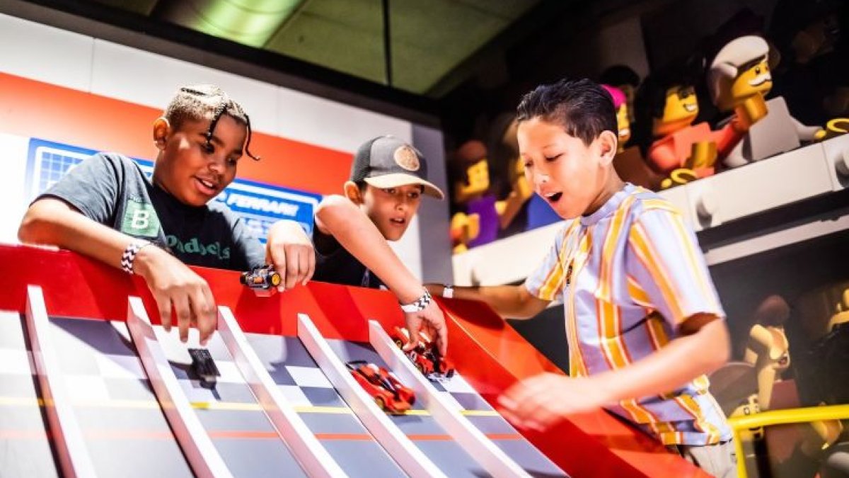 three kids racing small toy cars down ramp at Ferrari build and race at Legoland Florida.