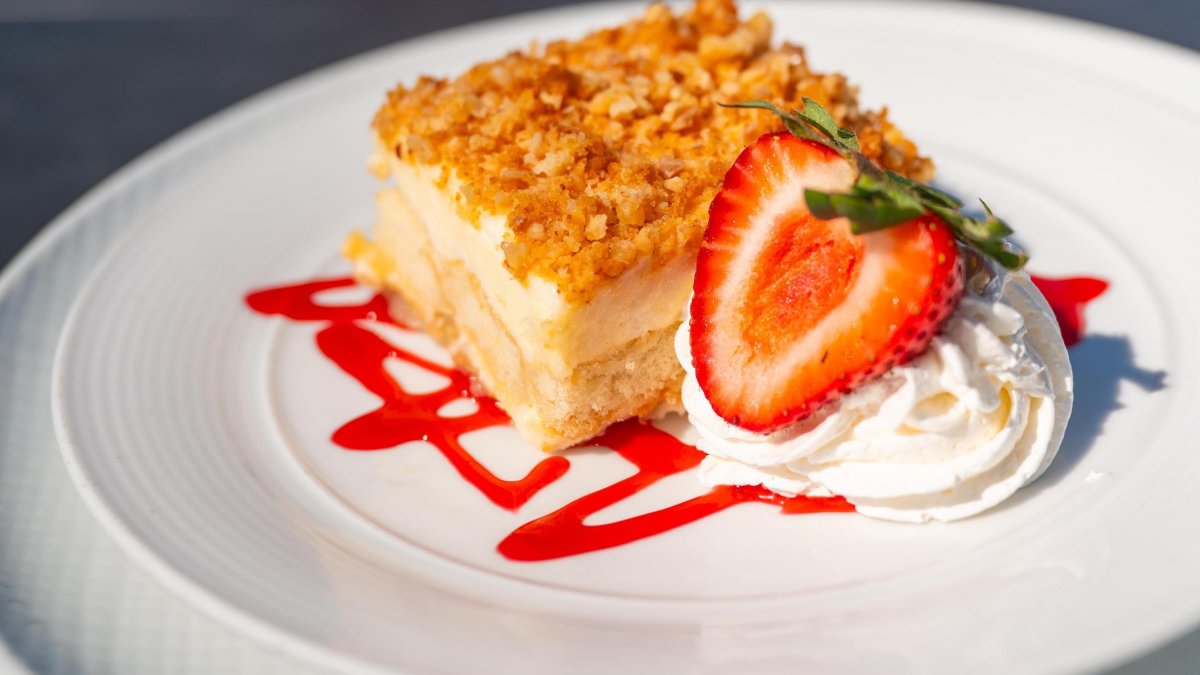 a square cheesecake slice with a crumble top, garnished with whipped cream and strawberries and a drizzle of strawberry sauce
