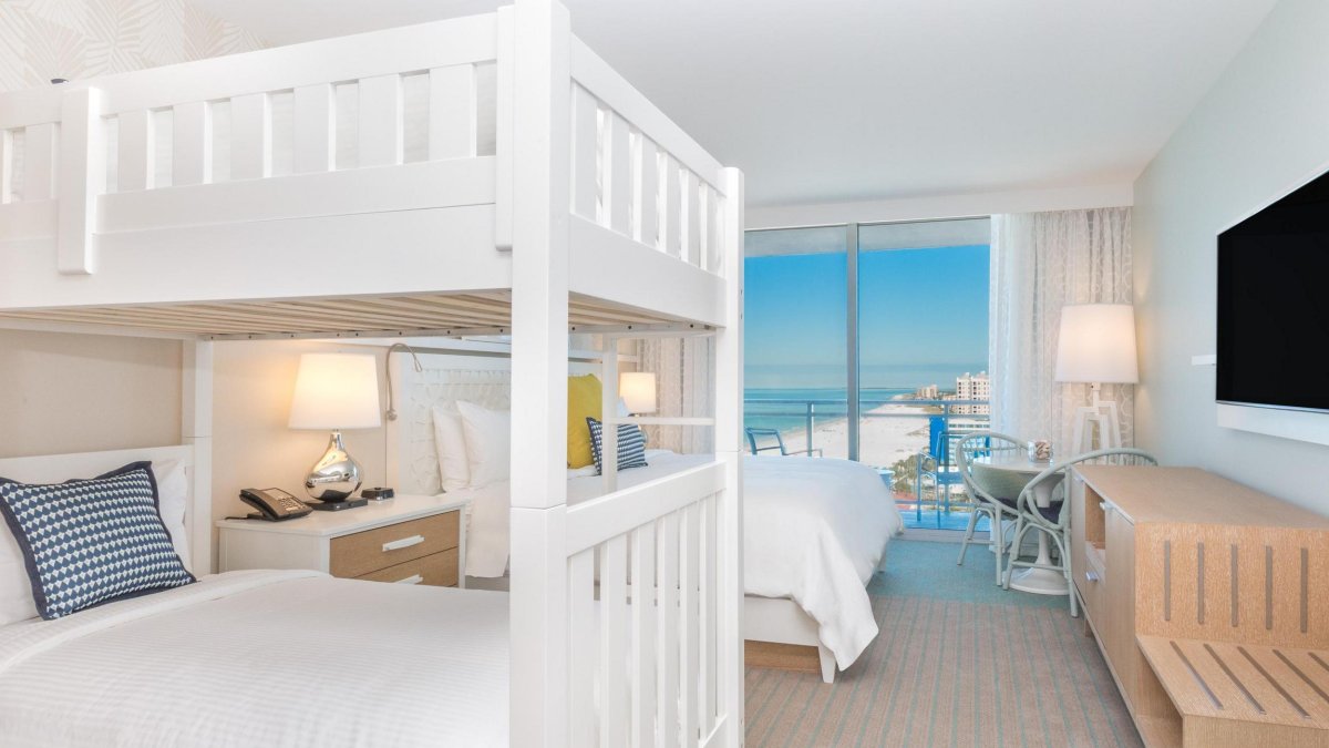 white bunk beds next to a white king bed in a hotel room overlooking the Gulf at Wyndham Grand Clearwater Beach