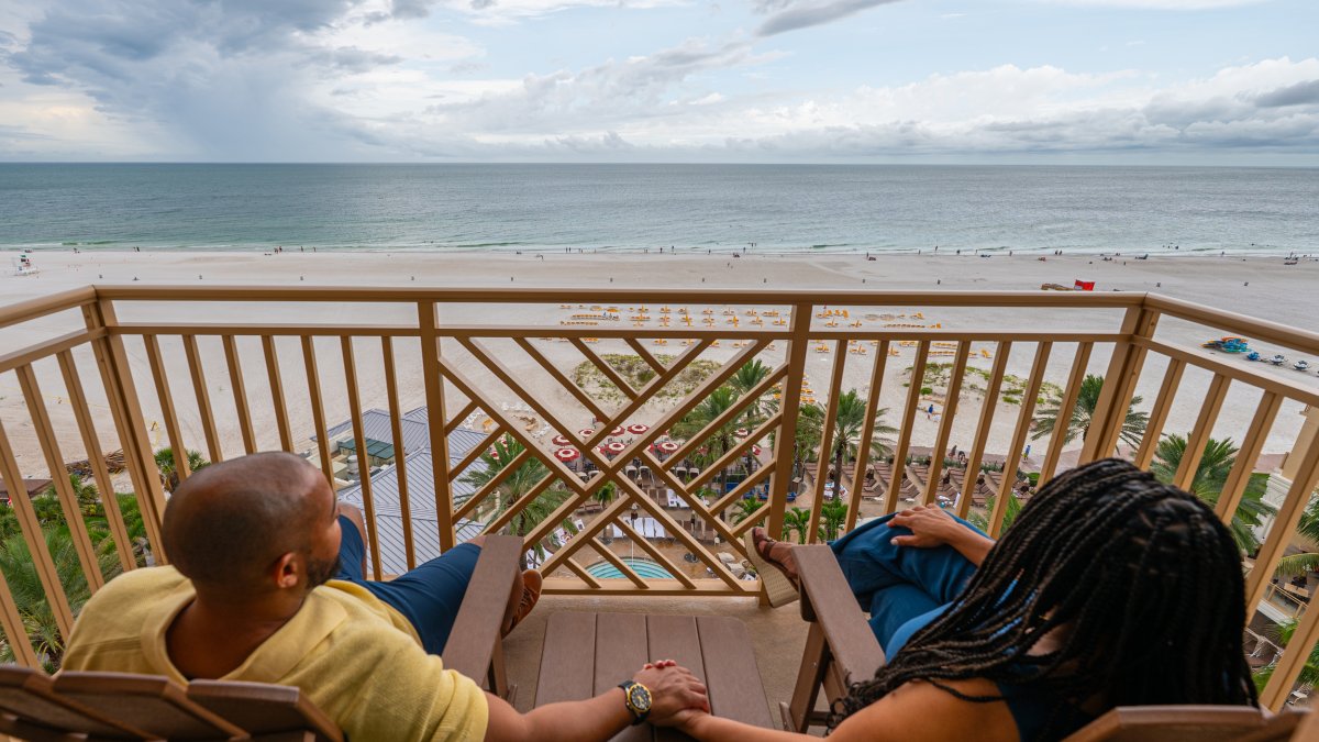 a couple holds hand while relaxing in chairs on a beachfront terrace at Sandpearl Resort