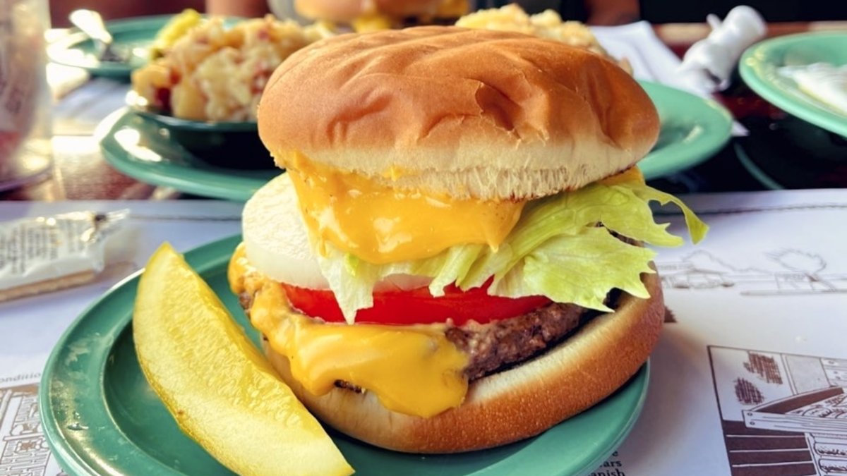 a cheeseburger with melted American cheese, onion, tomato and lettuce, next to a pickle wedge at Ted Peters Famous Smoked Fish